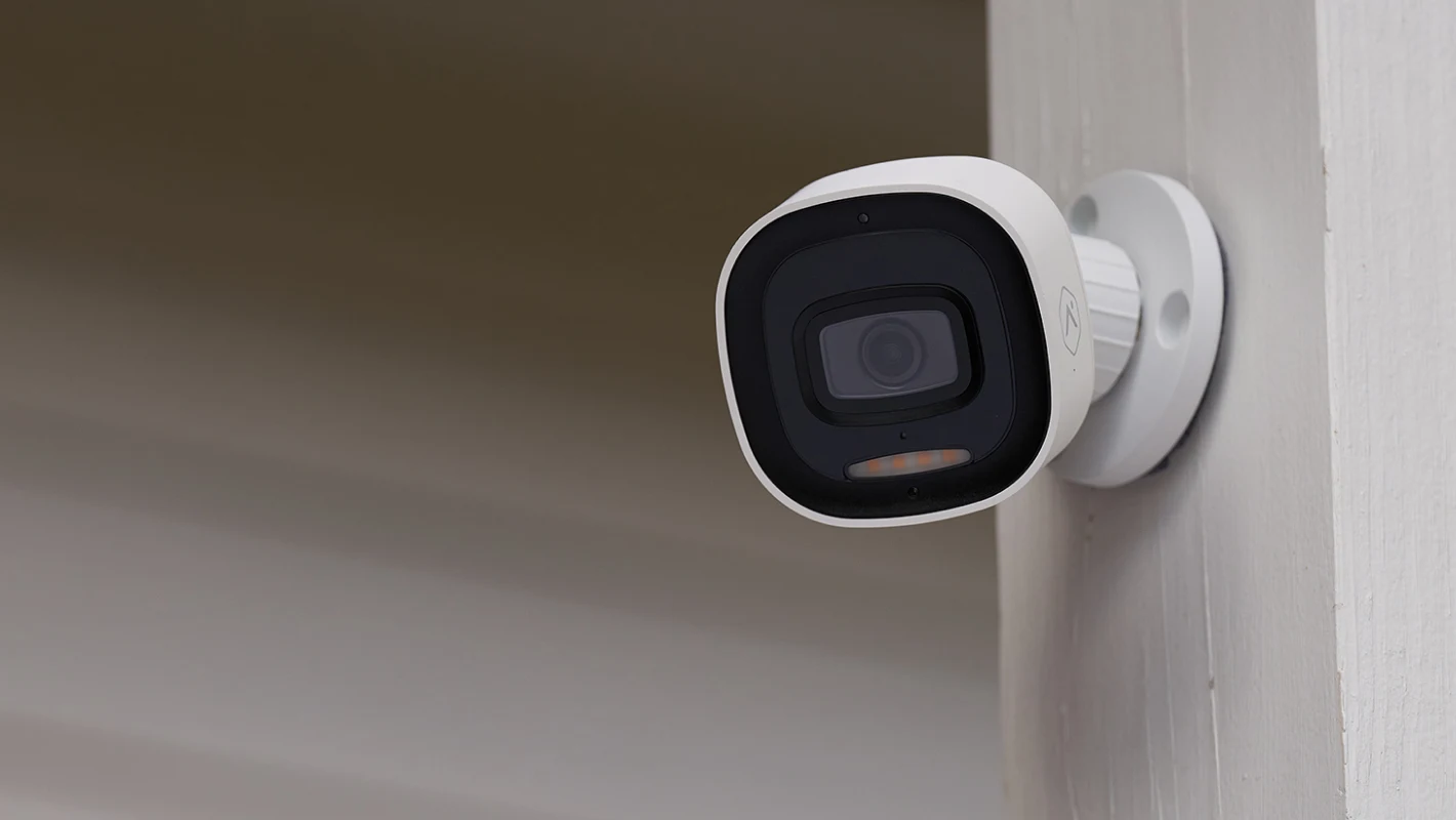 ADT outdoor Smart Camera with its front spotlight, clearly visible on a white exterior post in daylight
