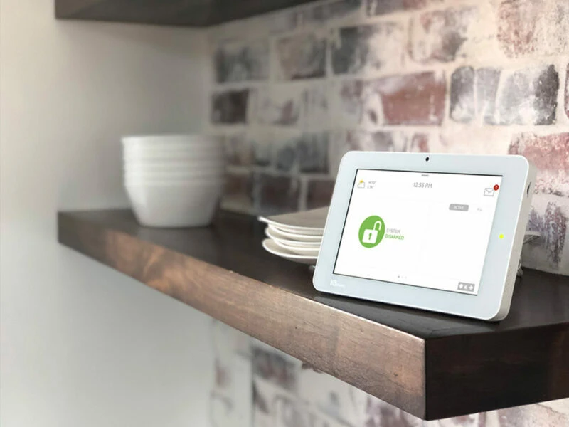 One white Qolsys touchscreen alarm panel on a kitchen shelf