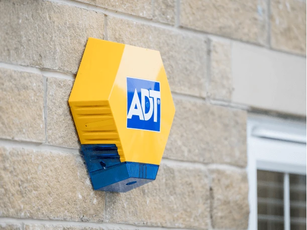 Yellow ADT decoy box fitted to the stone wall of a home beside a window