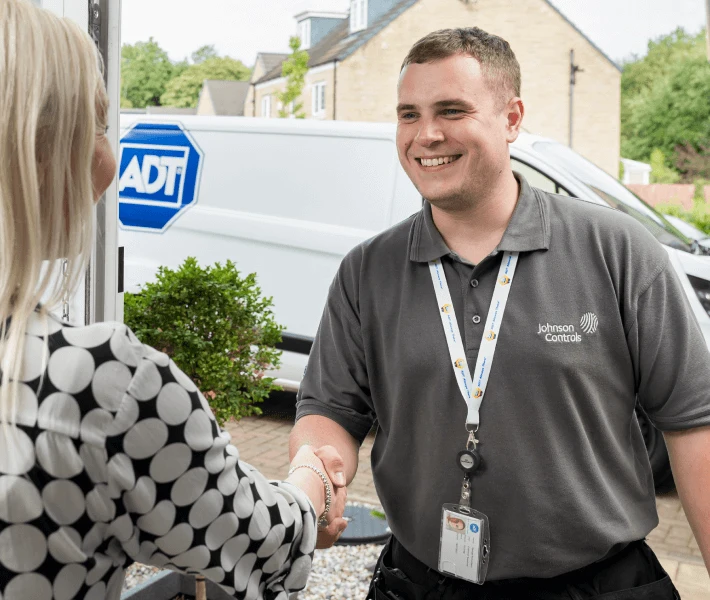 An ADT engineer greeting a homeowner at her front door, with the ADT van behind him
